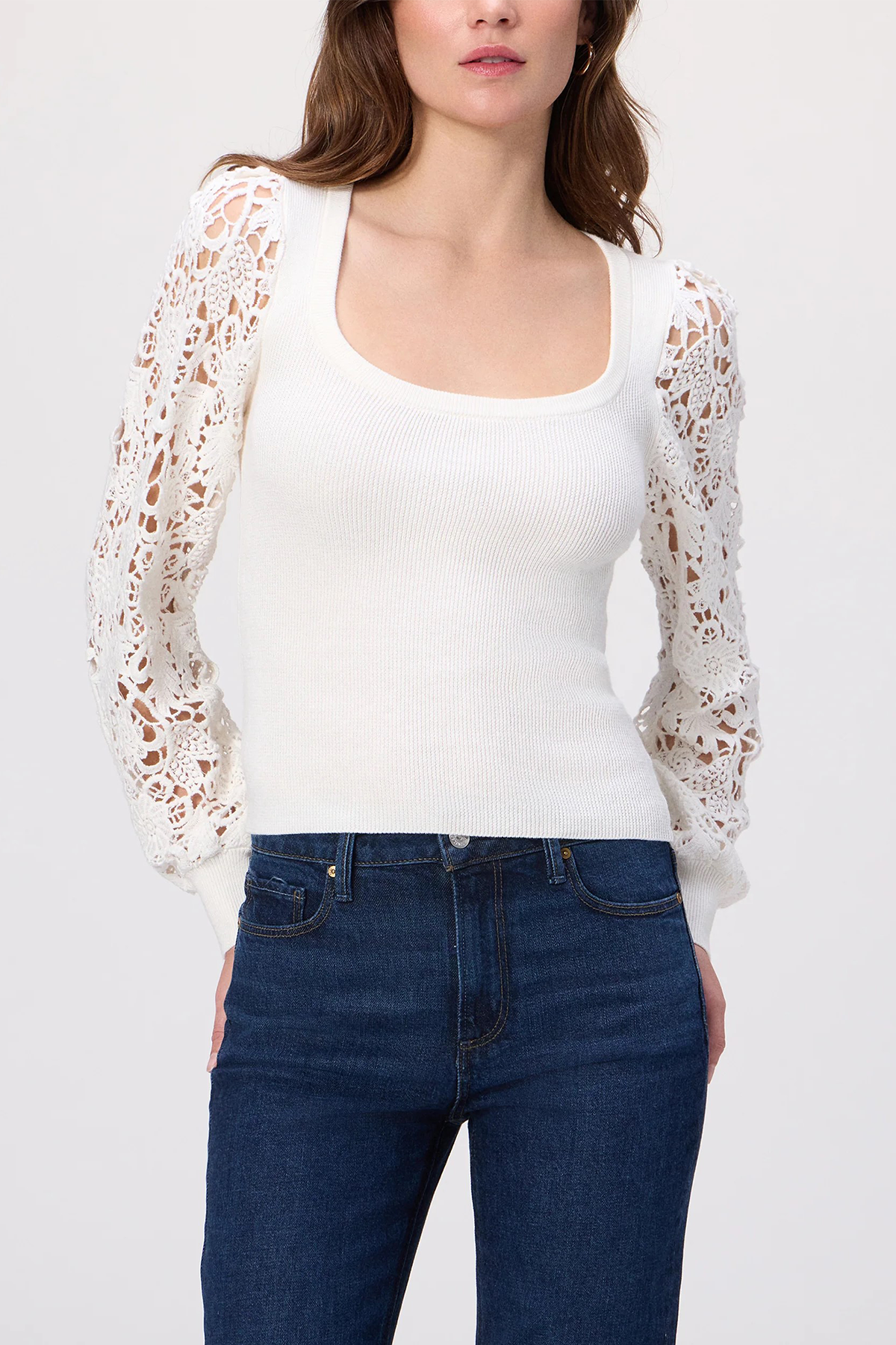 Woman wearing a white lace cardigan over a white top and blue jeans on a white background