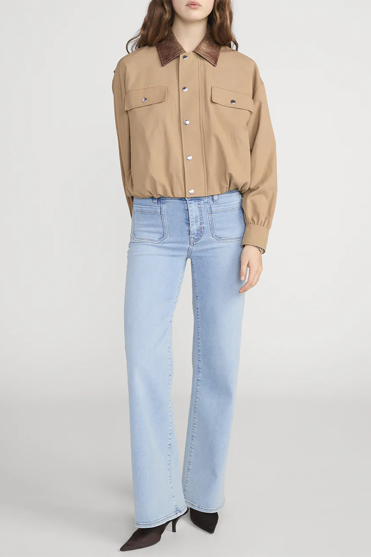 Person wearing a beige shirt with brown collar and light blue jeans on a white background