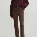 A model wearing a dark burgundy knit V-neck sweater and brown straight-leg jeans, paired with black pointed-toe heels, against a light gray studio background.