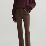 A model wearing a dark burgundy knit V-neck sweater and brown straight-leg jeans, paired with black pointed-toe heels, against a light gray studio background.