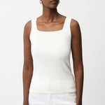 Woman wearing a white tank top and pants on a plain background