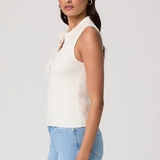 Woman wearing a white sleeveless top and light blue jeans on a plain background