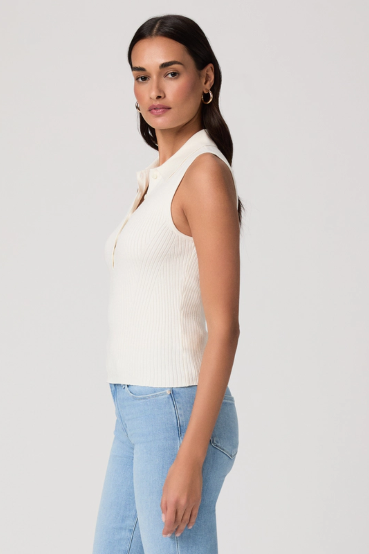 Woman wearing a white sleeveless top and light blue jeans on a plain background