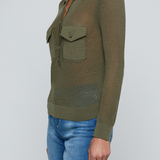 Model wearing a green knit button front sweater top with jeans on an off white background.