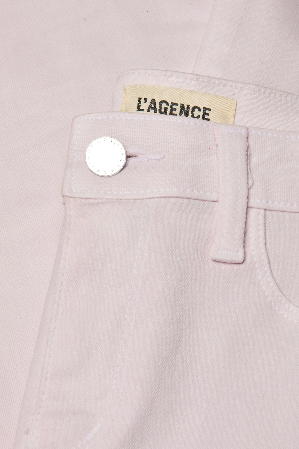 Close-up of a light pink garment with 'L'Agence' label and button detail.