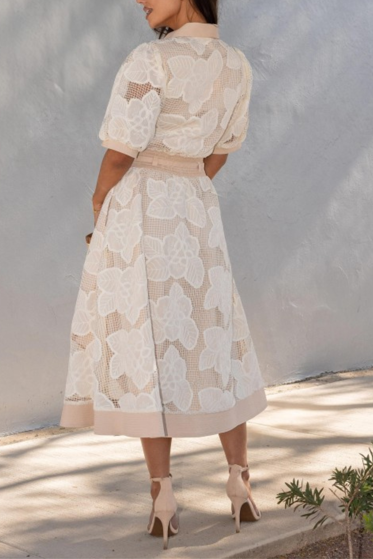 Woman wearing a beige lace dress against a white wall.