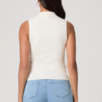 Woman wearing a white sleeveless top and light blue jeans on a plain background