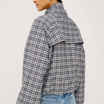 A woman shown from the back wearing a navy and white plaid cropped jacket with voluminous sleeves, paired with light blue jeans, against a plain light gray studio background.
