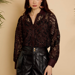 Woman wearing a dark patterned blouse and black leather shorts against a beige background