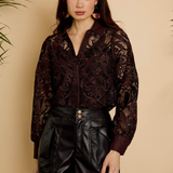 Woman wearing a dark patterned blouse and black leather shorts against a beige background