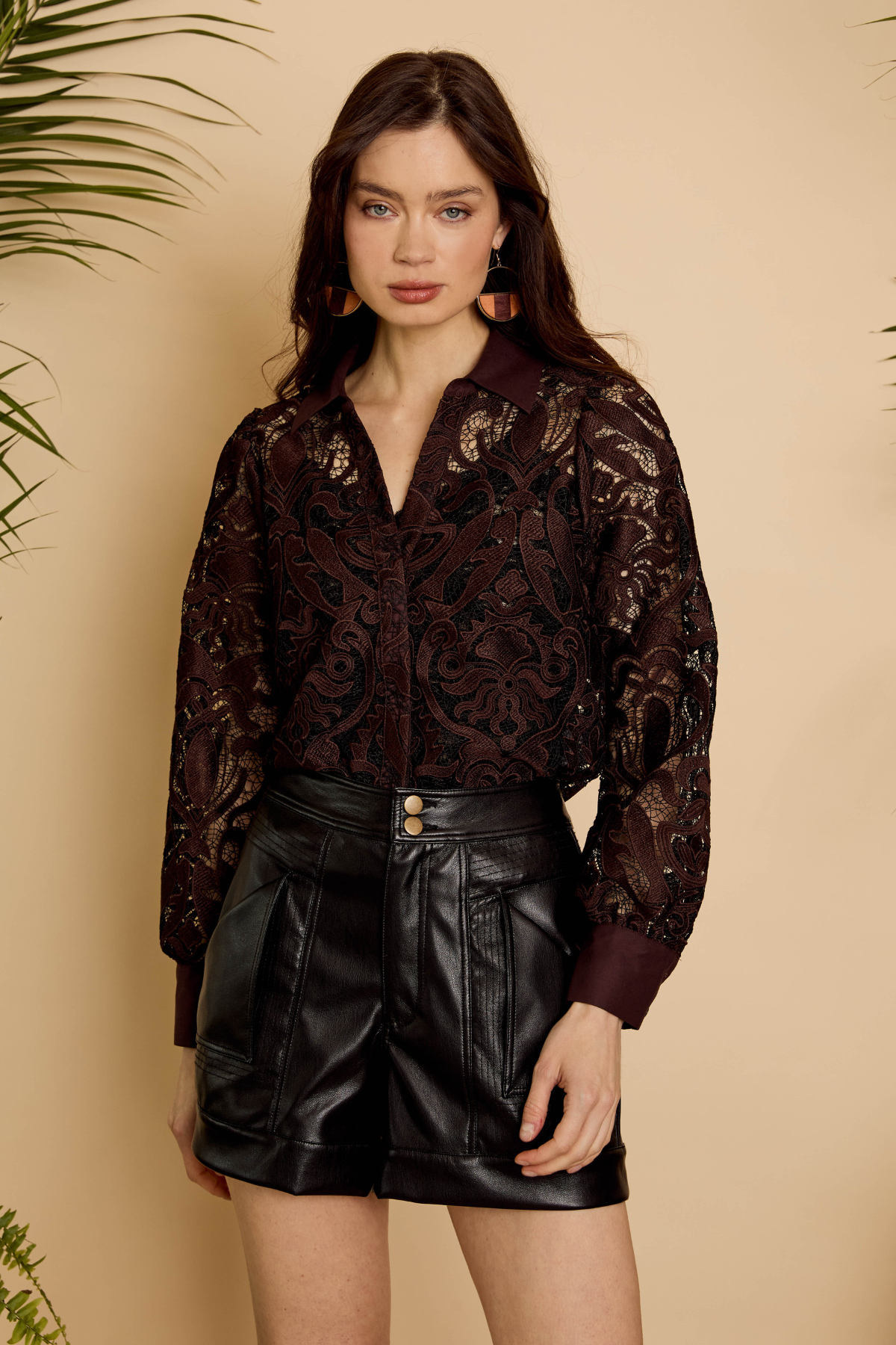 Woman wearing a dark patterned blouse and black leather shorts against a beige background