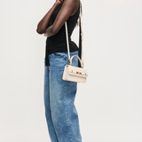 Woman wearing a black top and blue jeans with a white handbag on a white background