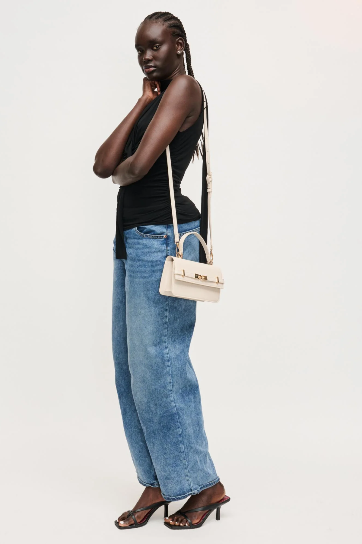 Woman wearing a black top and blue jeans with a white handbag on a white background