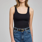 A woman modeling a black scoop-neck tank top paired with blue jeans and a black belt, photographed against a neutral light gray studio background.