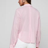 Woman wearing a pink pleated shirt and white shorts on a plain background