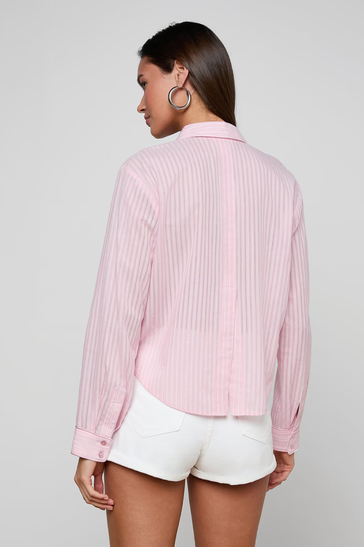 Woman wearing a pink pleated shirt and white shorts on a plain background