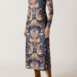 Woman wearing a long, patterned dress with brown boots on a white background