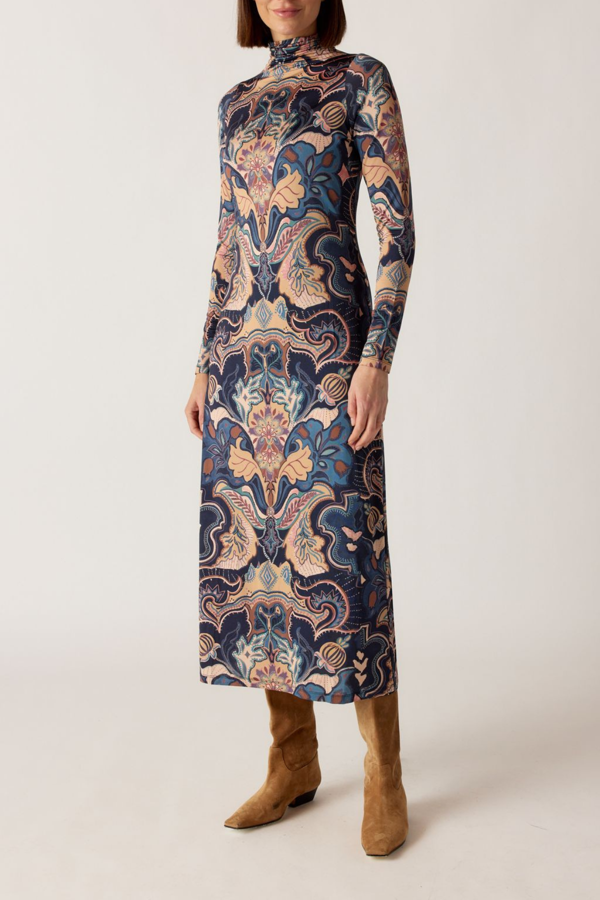 Woman wearing a long, patterned dress with brown boots on a white background