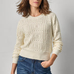 Woman wearing a cream knitted sweater and blue jeans against a gray background