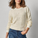 Woman wearing a cream knitted sweater and blue jeans against a gray background
