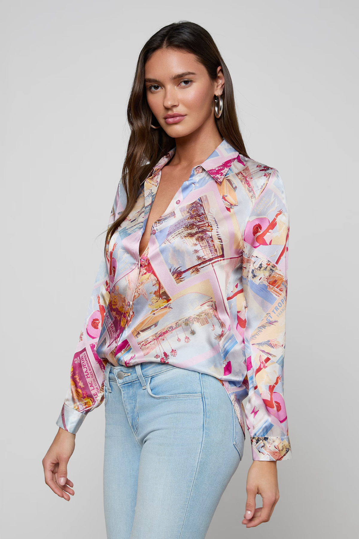 Woman wearing a colorful blouse with abstract patterns and light blue jeans on a plain background
