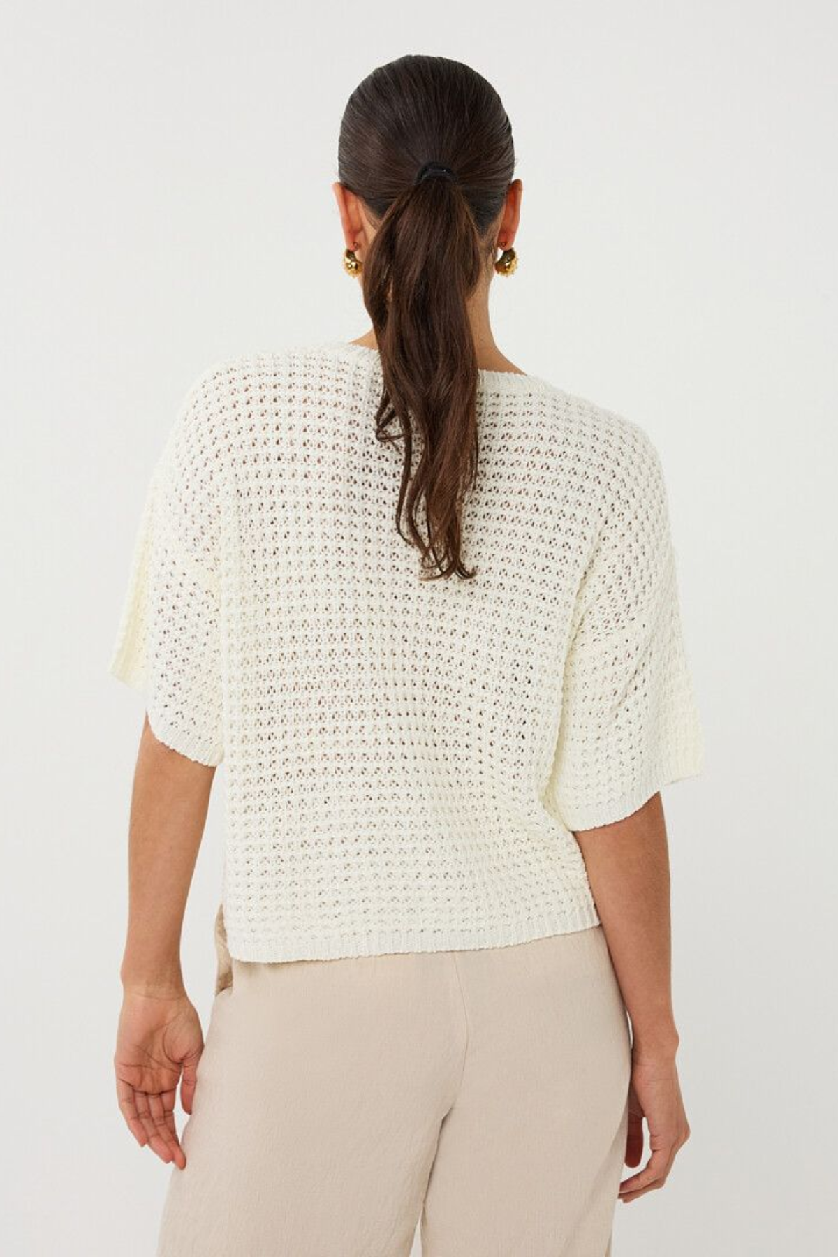 Woman wearing a white textured top and beige pants on a white background
