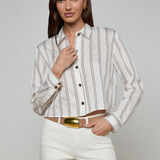 Woman wearing a striped shirt and white pants with a gold belt on a gray background