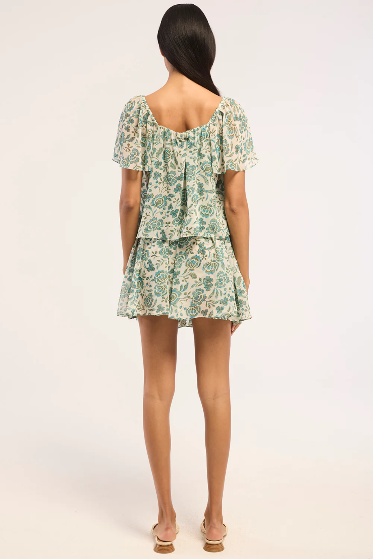 Woman wearing a floral top and skirt on a white background - back angle