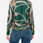A woman shown from the back wearing a green satin shirt jacket with a detailed horse bit and rope print, paired with blue jeans, against a light gray studio background.