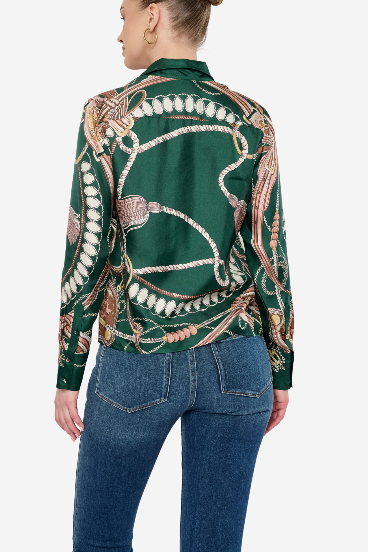 A woman shown from the back wearing a green satin shirt jacket with a detailed horse bit and rope print, paired with blue jeans, against a light gray studio background.