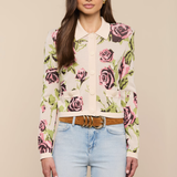 Woman wearing a floral blouse and light blue jeans against a beige background