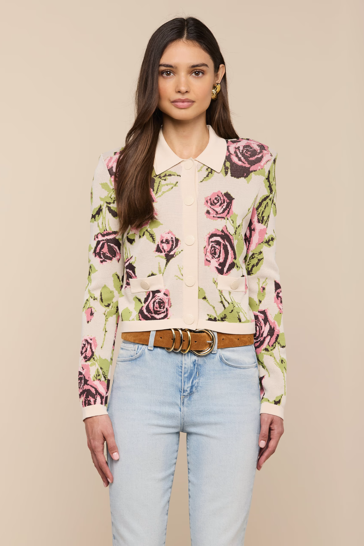 Woman wearing a floral blouse and light blue jeans against a beige background