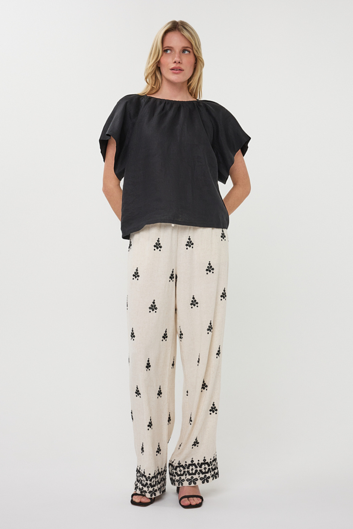 Woman wearing a black top and patterned pants on a white background