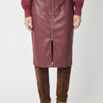 A model is shown from the chest down wearing a knee-length burgundy faux-leather skirt with a front zipper, paired with a matching burgundy top and brown suede over-the-knee boots, against a plain white studio background.