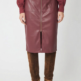 A model is shown from the chest down wearing a knee-length burgundy faux-leather skirt with a front zipper, paired with a matching burgundy top and brown suede over-the-knee boots, against a plain white studio background.