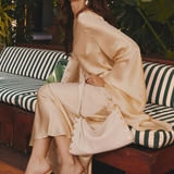 Woman in beige outfit sitting on a striped bench with greenery in the background