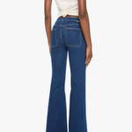 A model shown from the back wearing dark blue high-waisted flare jeans and a cream-colored wrap top, set against a plain white studio background.