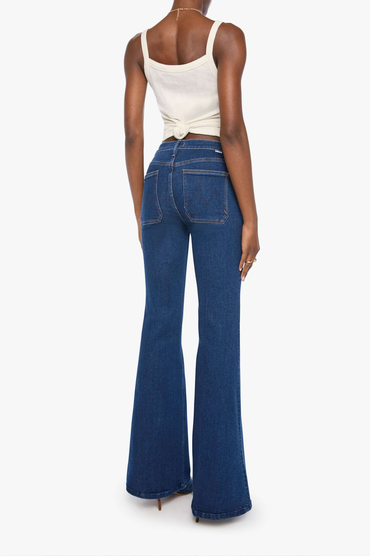 A model shown from the back wearing dark blue high-waisted flare jeans and a cream-colored wrap top, set against a plain white studio background.