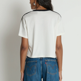 Person wearing a white t-shirt with black trim and blue jeans on a plain background
