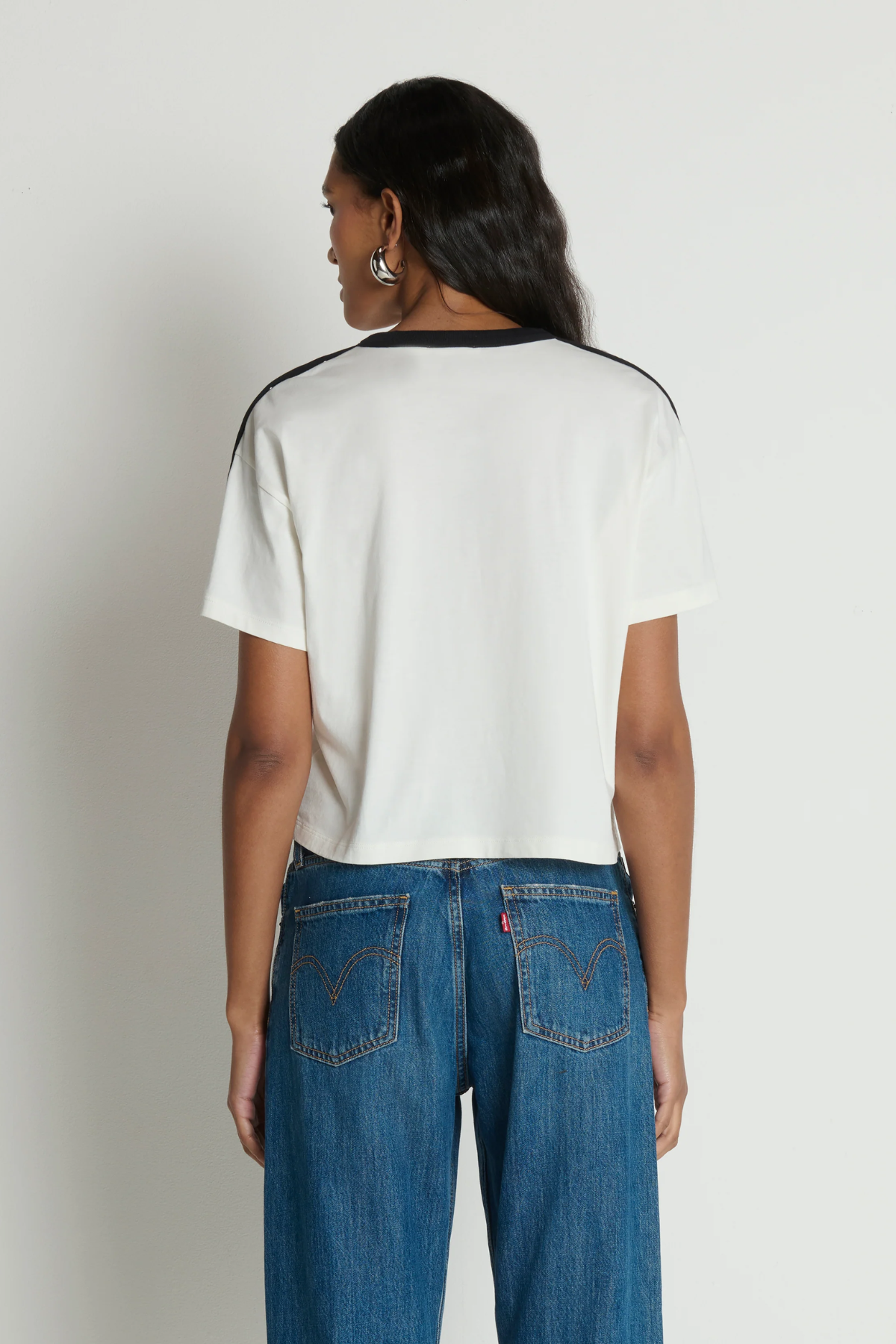 Person wearing a white t-shirt with black trim and blue jeans on a plain background