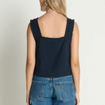 Woman wearing a navy tank top and blue jeans on a plain background