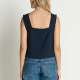 Woman wearing a navy tank top and blue jeans on a plain background