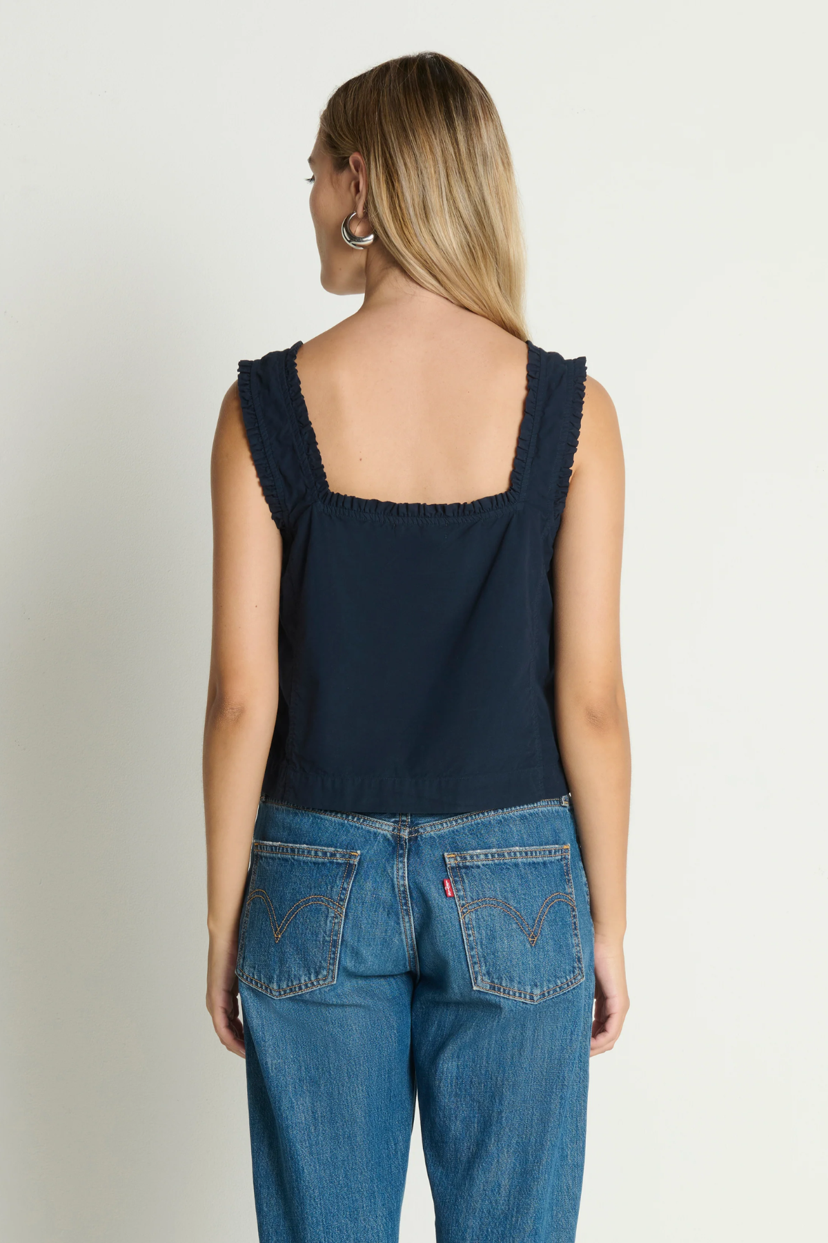 Woman wearing a navy tank top and blue jeans on a plain background