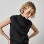A woman wearing a black ribbed sleeveless mock-neck sweater vest, shown from the waist up against a plain light gray studio background.