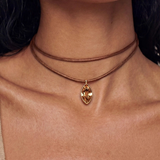 A close-up of a model wearing a double-strand brown cord choker necklace with a gold-toned marquise-shaped pendant containing a faceted amber gemstone.