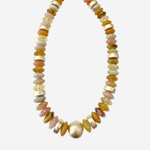 A beaded necklace featuring a mix of polished gold, amber, pink, and cream-colored stones, with a prominent textured gold bead at the center, displayed on a light gray background.