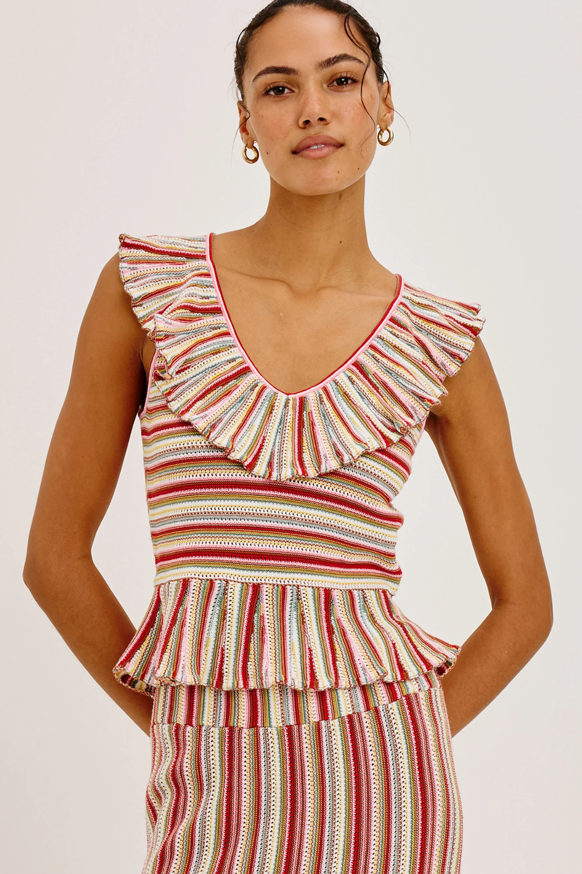 Woman wearing a striped sleeveless top with ruffled details on a white background