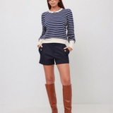 A woman modeling a navy and white striped long-sleeve knit top, navy shorts, and brown knee-high leather boots against a plain light gray studio background.