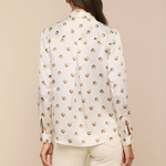 Woman wearing a white blouse with gold heart patterns on a beige background