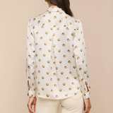 Woman wearing a white blouse with gold heart patterns on a beige background